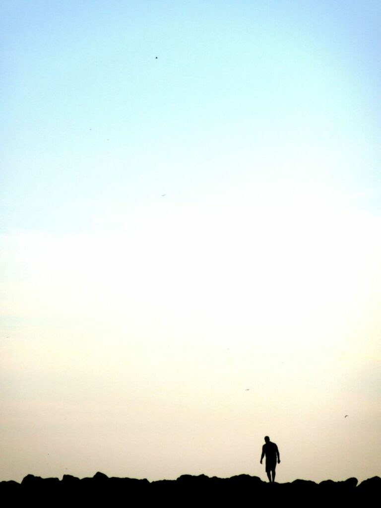 Un homme, sa silhouette ou son ombre, marche sur une jetée de pierres à hauteur de Corbières à Marseille.