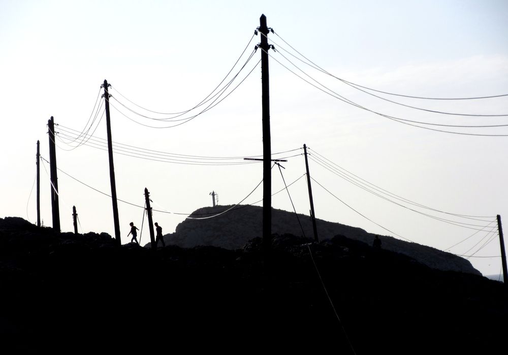 Deux ombres marchent sur une hauteur des Goudes à Marseille. Ils sont entourés de fils et de poteaux électriques.