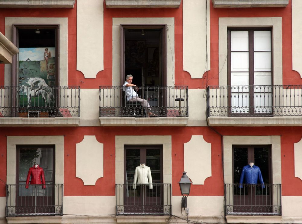 Un homme à son balcon regarde vers l'horizon. Des mannequins sans tête se trouvent à l'extérieur dans les autres étages.