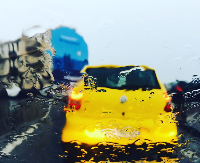 Une voiture jaune circule vers les Catalans à Marseille. La photo est prise derrière une vitre mouillée par la pluie.