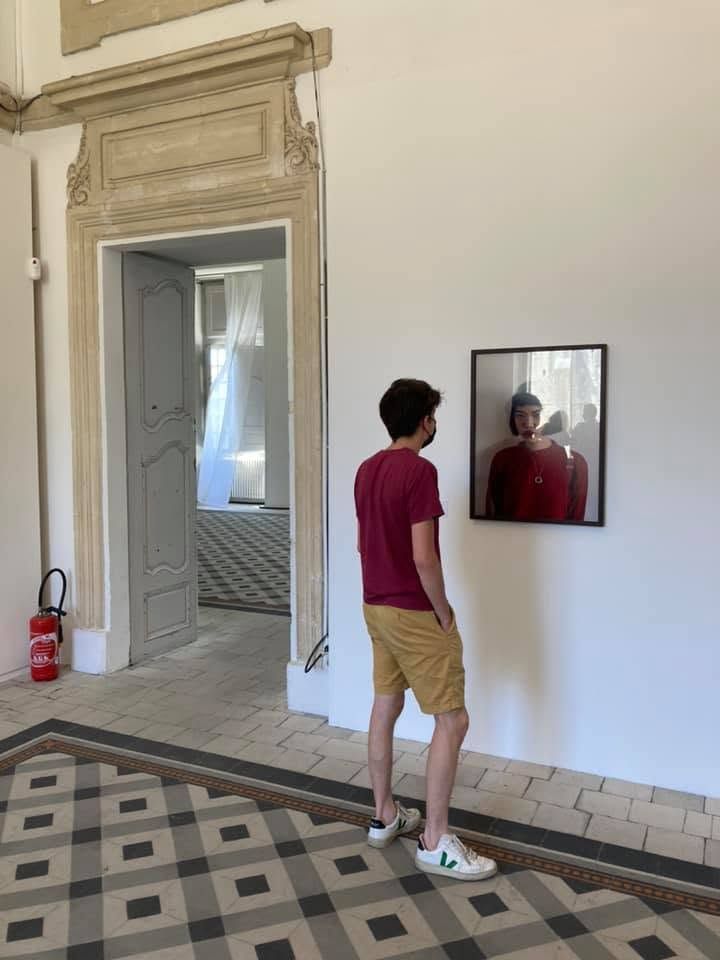 Un jeune homme regarde une photo avec laquelle sa tenue rouge semble se mélanger. Effet de miroir.