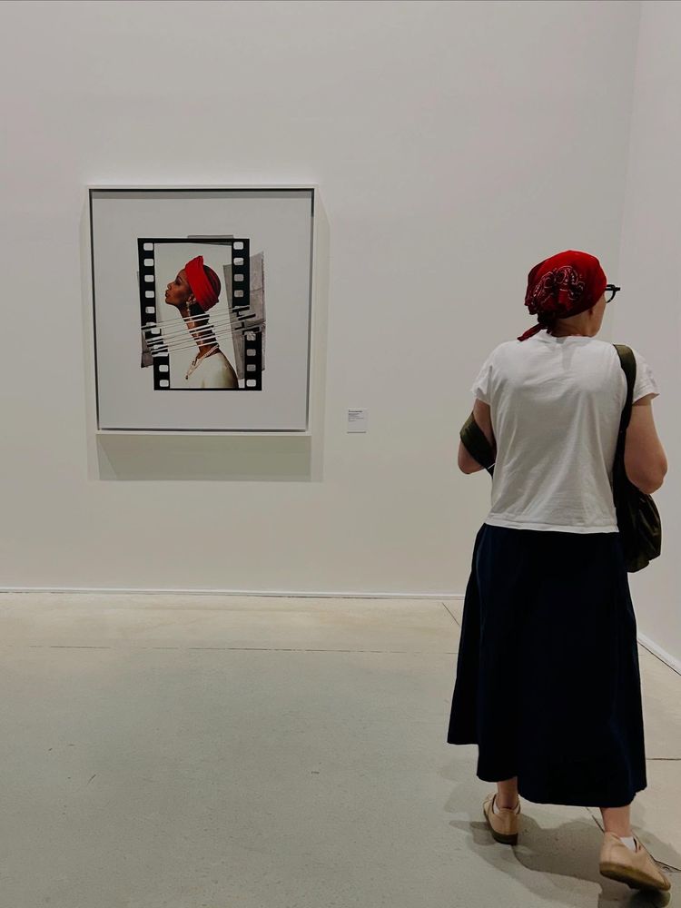 Une femme, avec un tissu rouge sur la tête, se trouve près d'une photo dans laquelle il y a une dominante de couleur rouge.