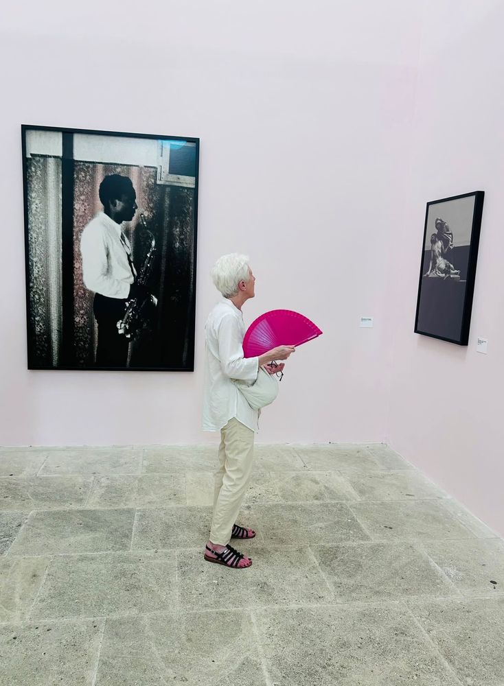 Une femme, avec un éventail rose, regarde des photos aux Rencontres de la photographie à Arles en 2026.