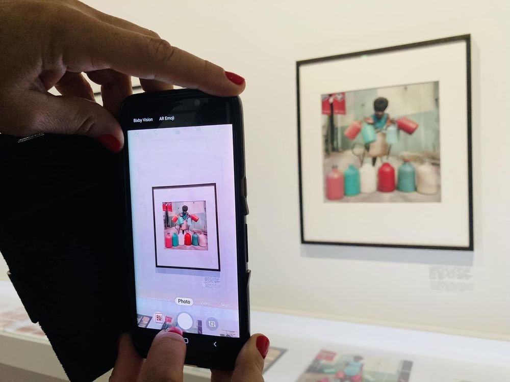 Une femme aux ongles rouges prend une photo d'une photo de James Barnor. Les Rencontres de la photographie d'Arles en 2024.